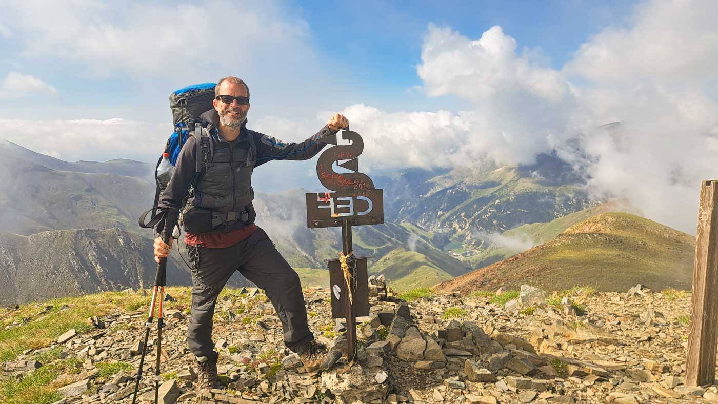 Etapa 10: Cabaña de Tirapits - Font dels Plaus. Transpirenaica GR11. 2 Caminante en n lo alto de la montaña junto a señal en la cresta del Valle de Nuria