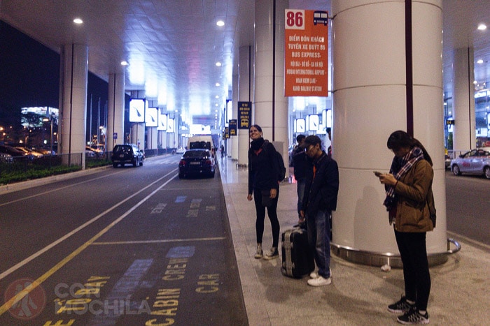 Carme at the Express Bus 86 stop at Hanoi Airport (with the old sign). The terminal is visible on the right.