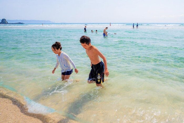 Pareja japonesa chapoteando en el agua, ella con manga larga