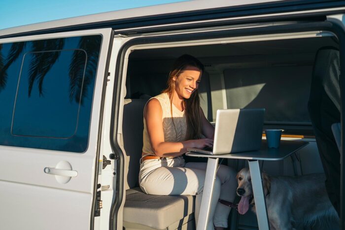 Holafly Plans: para quién merece la pena la suscripción 1 Viajera trabajando con el portátil desde una furgoneta camper, con su perro al lado