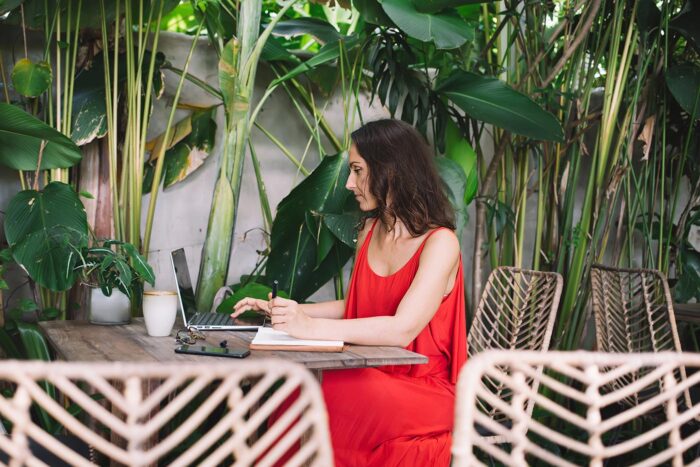 Holafly Plans: para quién merece la pena la suscripción 2 Viajera trabajando con el portátil en una terraza tropical, con el móvil sobre la mesa